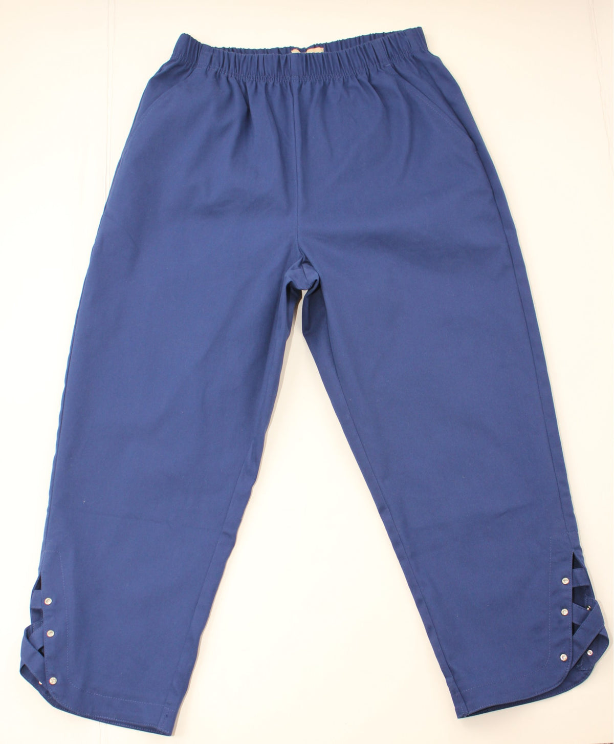 A pair of blue cropped pants with an elastic waistband and decorative cutout details on the lower hems, laid flat against a light background.