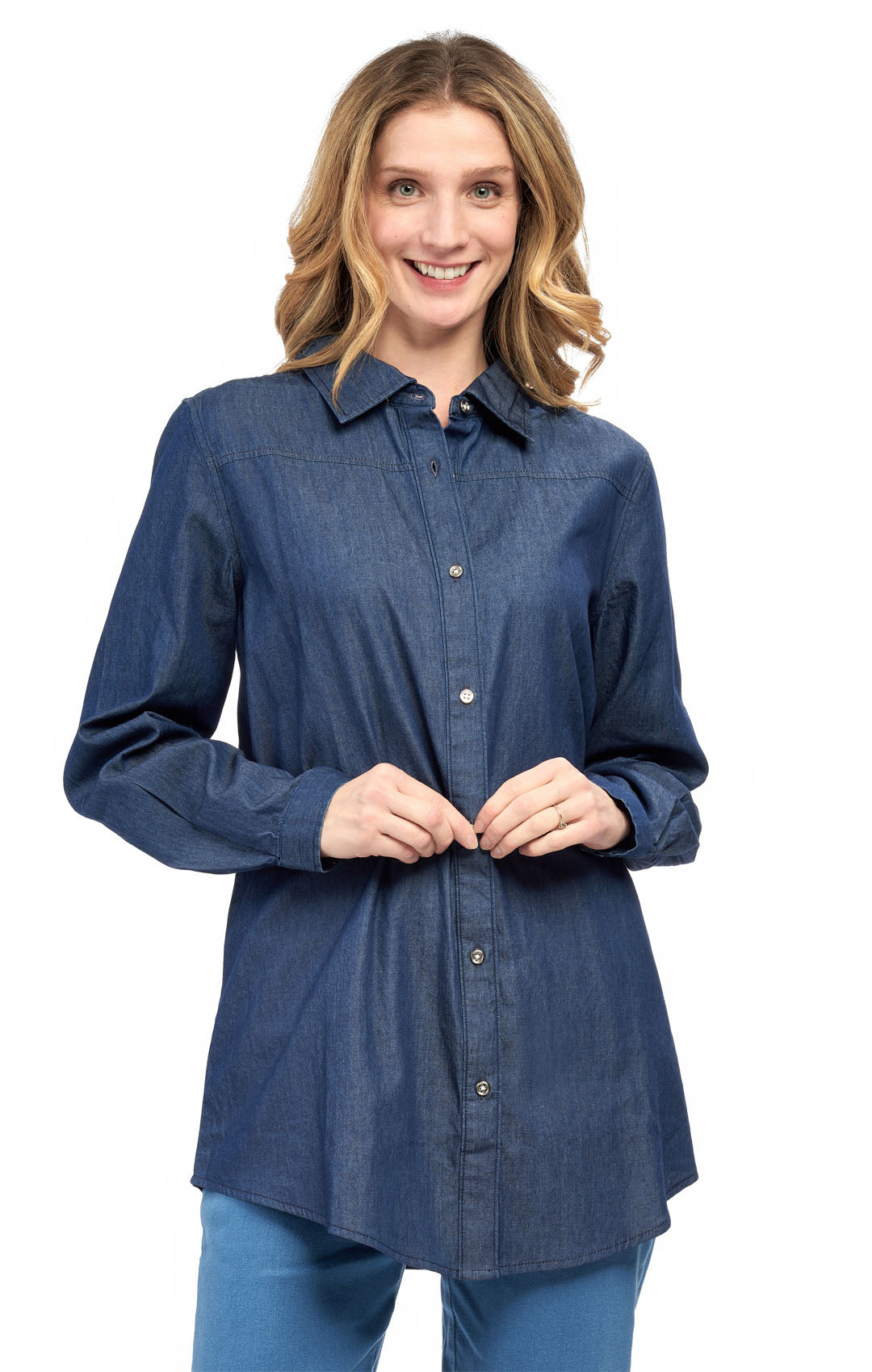 A woman wearing a long sleeve denim tunic top with a collar, button cuffs, and a shirttail hem.